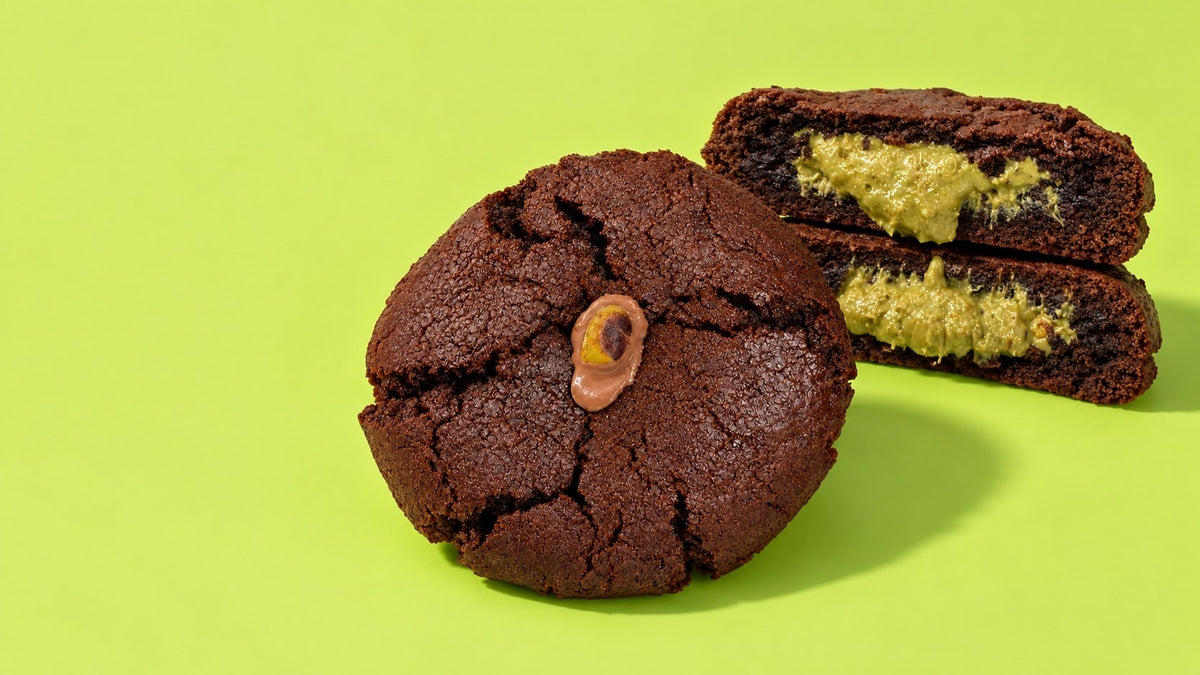 The Dubai Cookie, one whole and two halves showing the pistachio knafeh inside, on pistachio green